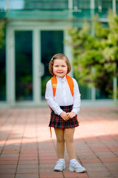a small beautiful girl stands near the school building, with a backpack - Fotografie, Obrázek