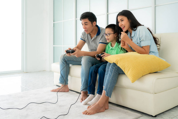 Asiatique père de famille et fils s'amuser à jouer à des jeux de console d'ordinateur ensemble dans le salon à la maison avec des contrôleurs de combiné et la mère encourage les joueurs
 - Photo, image