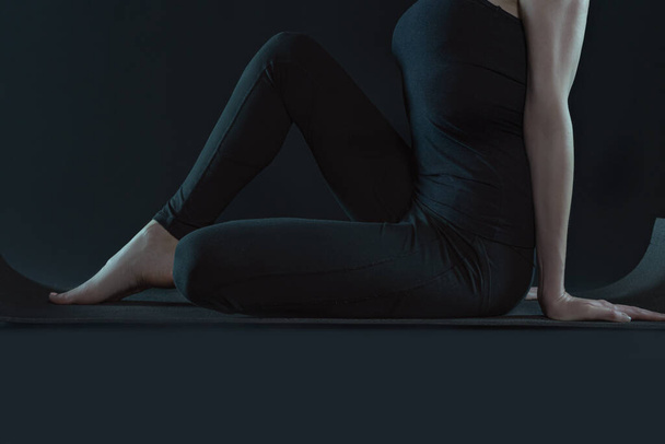 Young woman practicing yoga position stretching .yoga mat and leggins on a dark black background. copy space. sport workout fitness exercise. - Photo, Image