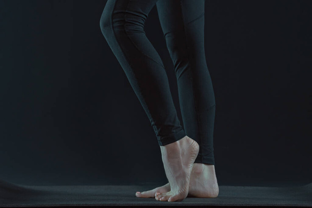 Gambe di giovane donna che praticano yoga su stuoia di yoga su uno sfondo nero scuro. copia spazio
. - Foto, immagini