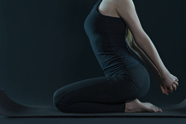 Молодая женщина практикует позицию yoga растягивая циновку .yoga и leggins на темном черном фоне. скопировать пространство. фитнес-упражнения
. - Фото, изображение