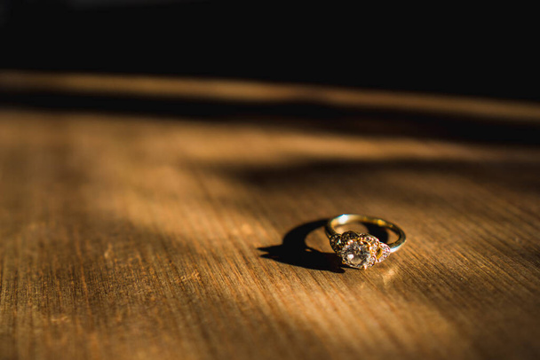 Een gouden diamanten verlovingsring zat op een houten tafel bij daglicht - Foto, afbeelding