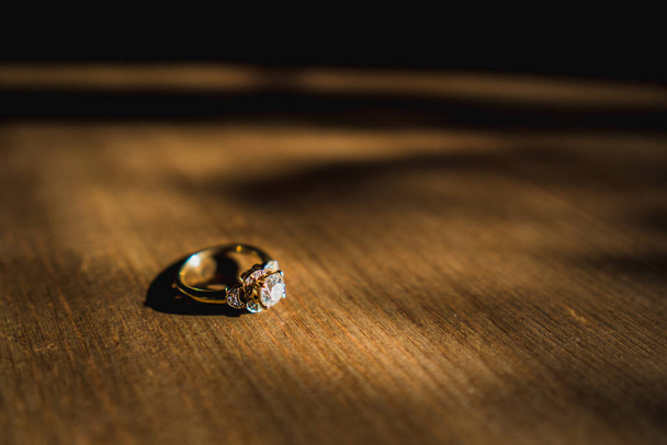 Een gouden diamanten verlovingsring zat op een houten tafel bij daglicht - Foto, afbeelding