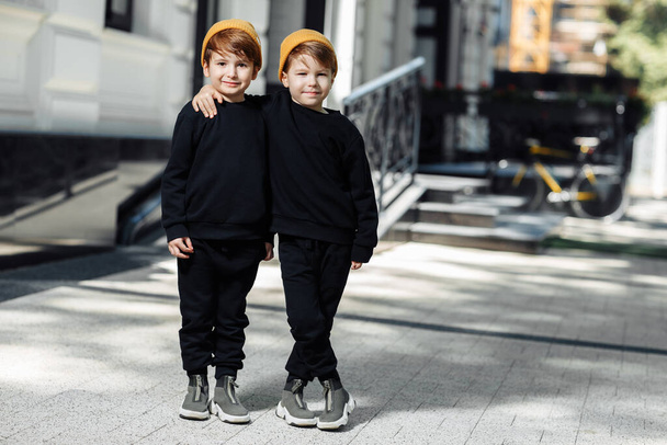 Two cheerful embraced twin boys posing with happy faces in the street. - Фото, зображення
