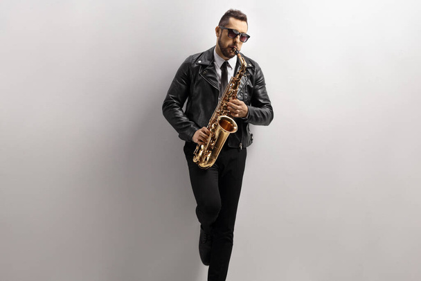Man playing a saxophone and leaning on a gray wall - Foto, immagini