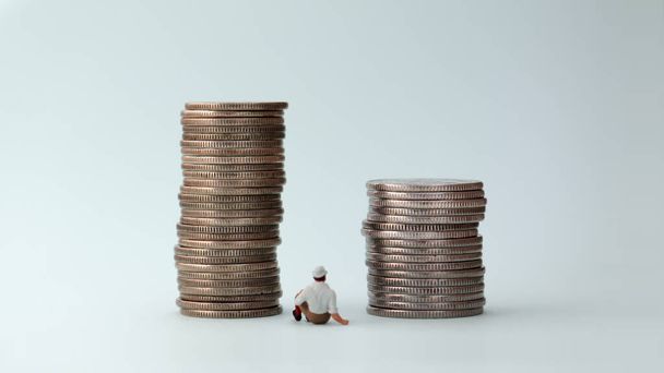 Мініатюрна людина сидить між двома кулями монет
. - Фото, зображення