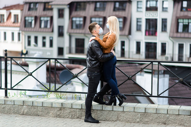 Молодая пара влюблена в защитную медицинскую маску на открытом воздухе на улице. Парень и девушка в защите от вирусов. - Фото, изображение