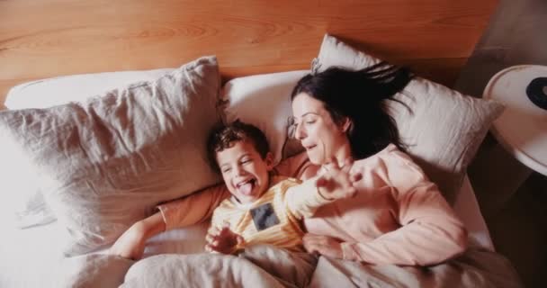 Young mother and son relaxing and having fun in bed - Imágenes, Vídeo