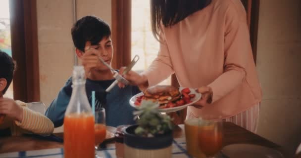 Mother serving pancakes with strawberries to son as breakfast - Materiał filmowy, wideo