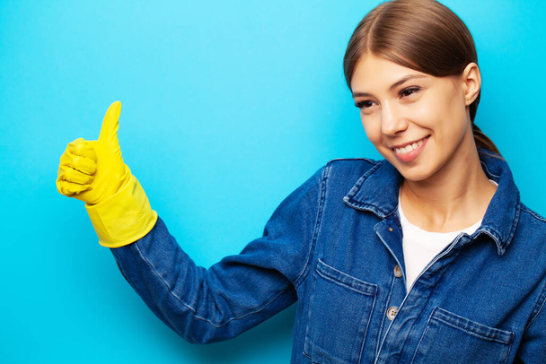 Egy takarítócég alkalmazottja overálban és sárga kesztyűben, kék alapon pózolva. - Fotó, kép