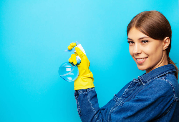 Temizlik şirketi çalışanı, sarı eldivenler ve mavi arka planda duran temizlik malzemeleri. - Fotoğraf, Görsel