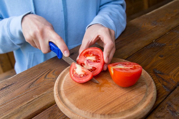 木のテーブルの上でトマトを切った女の子の手、ベジタリアンサラダを作るプロセス、野菜や緑のクローズアップカット - 写真・画像