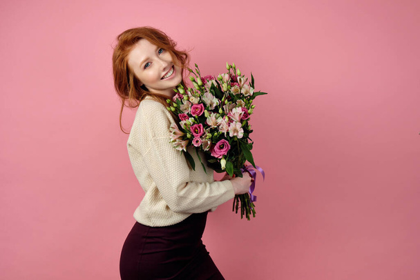 Cute red-haired girl is standing in a half-turn on a pink backgr - Φωτογραφία, εικόνα