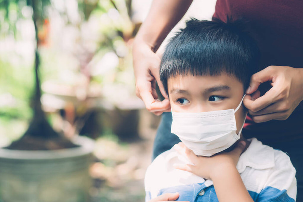 Äiti huolehtia poika kasvonaamio suojaava tauti flunssa tai covid-19 ulkona, äiti yllään lääketieteellinen naamio lasten turvallisuutta suojella puhkeamista pandemian julkisesti, lääketieteellinen käsite. - Valokuva, kuva