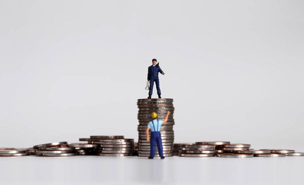 Мініатюрна людина з гучномовцем на купі монет і мініатюрною людиною, що стоїть під монетою
. - Фото, зображення
