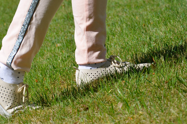 Die Füße des Mädchens laufen in Turnschuhen über das grüne Gras. Ein Teenager in Sportschuhen auf dem Rasen. Aktivitäten im Freien. Konzept: ein selbstbewusster, entschlossener Schritt nach vorn (in die Zukunft), das Erreichen des Ziels. - Foto, Bild