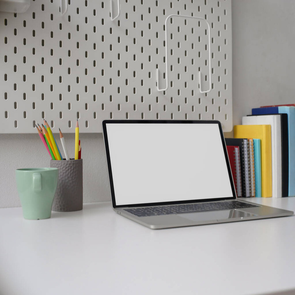 Imagen recortada de la oficina del hogar con estilo con el ordenador portátil de pantalla en blanco, taza, papelería y libros en la mesa blanca
 - Foto, Imagen