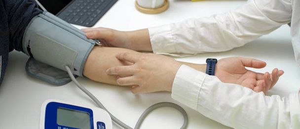 Tiro recortado do médico check-up médico seu paciente com monitor de pressão arterial na sala de exame
 - Foto, Imagem