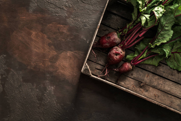 Свекла в деревянной коробке на темном фоне. Свежие овощи, здоровые органические продукты питания, урожай, сельское хозяйство, вид сверху
 - Фото, изображение