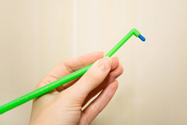 Cepillo de dientes verde con un mechón para tirantes en la mano de la mujer. El concepto de cuidado dental
. - Foto, Imagen