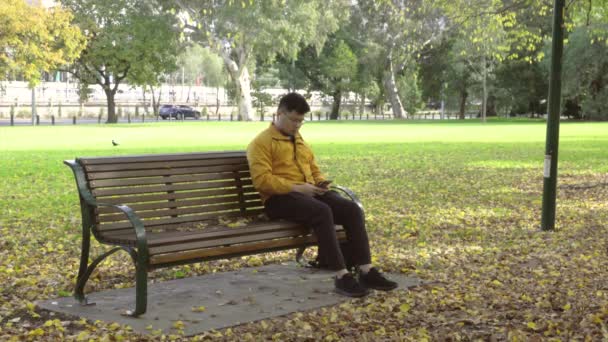 秋の公園でスマートフォンを使用して黄色のジャケットを持つ一人の男性. - 映像、動画
