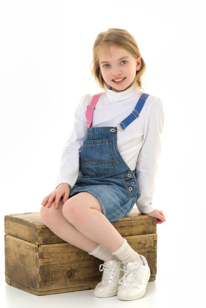 A little girl is sitting on a wooden box. - Фото, зображення