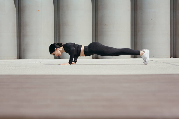 Fitness trainer doing morning push-up exercises on the street in park on the promenade against the background of concrete pipes. - Photo, Image
