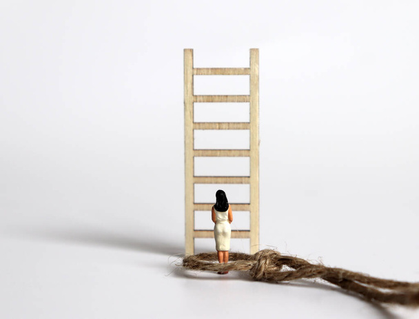Une femme miniature debout devant une échelle en bois. - Photo, image