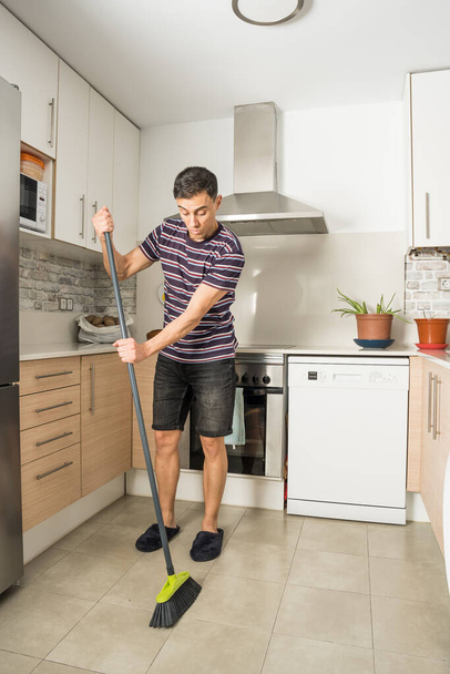 Man in casual clothes and slippers sweeping the kitchen floor. Full body. - Φωτογραφία, εικόνα