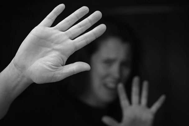 Избитая женщина защищает себя руками, крича о помощи из темноты.
. - Фото, изображение