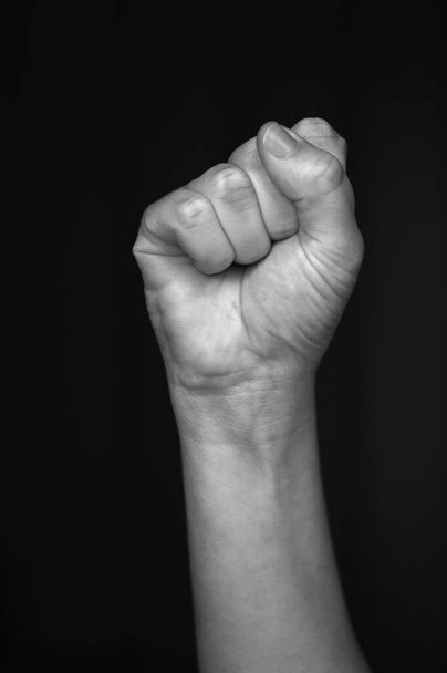 Женщина подняла кулак на черном фоне. Сжатый кулак является символом единства и умиротворения, а также салютом, выражающим единство, силу, неповиновение или сопротивление.
. - Фото, изображение