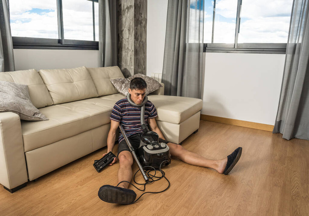 Man sitting on the floor in the living room trying to understand how a vacuum cleaner works. Full body. - Foto, imagen