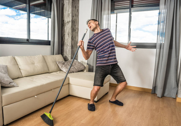 Man singing in the living room of his house holding the broom as if it were a microphone. Full body. - Fotoğraf, Görsel