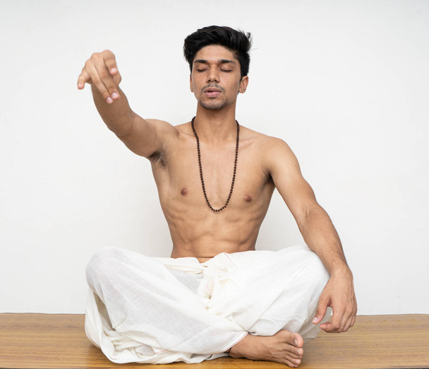Young indian priest sitting in dhoti, wearing rudraksh, showing up his hand representing giving should be the human nature. - Fotografie, Obrázek