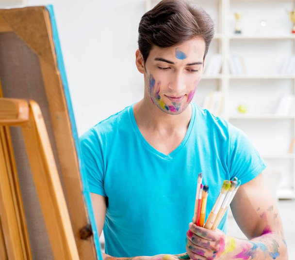 Jonge grappige kunstenaar werkt aan nieuw schilderij in zijn atelier - Foto, afbeelding