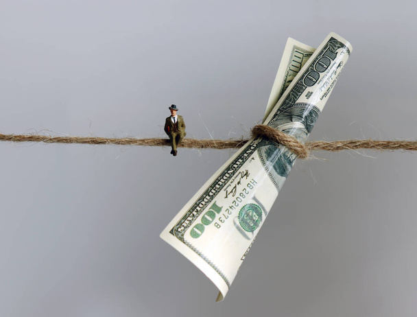 A miniature man sitting next to a $100 bill hanging from a rope. - Photo, Image