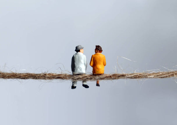 De achterkant van een miniatuur bejaard echtpaar zittend op een touw. Het begrip ouderdom en armoede. - Foto, afbeelding
