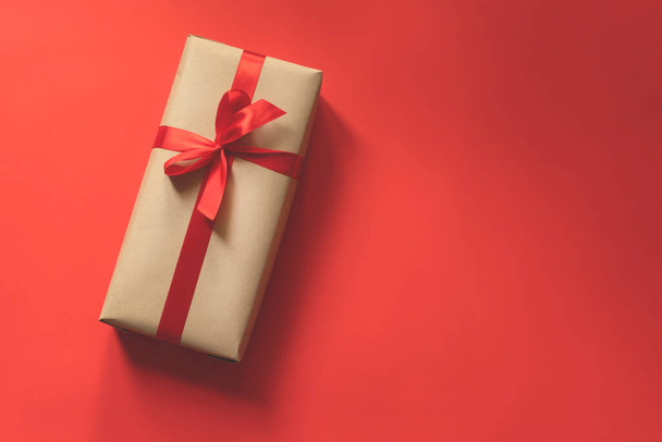 scatola regalo avvolta in carta normale con un nastro rosso su sfondo rosso
 - Foto, immagini