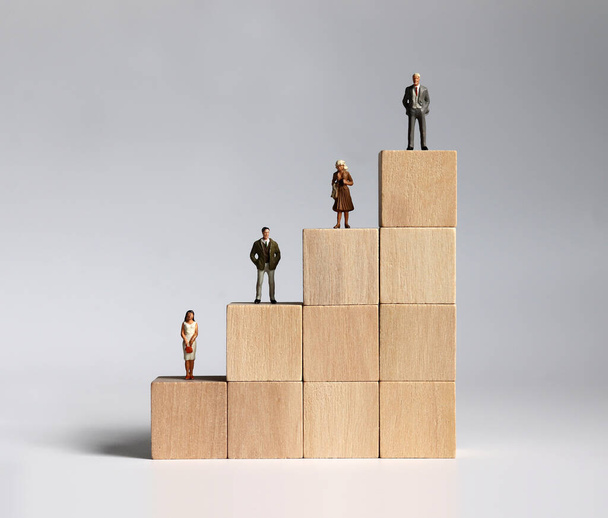 木製のブロックとミニチュアの人々。会社における男女差別の概念. - 写真・画像