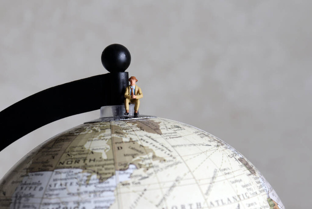 Een miniatuur man zittend op een wereldbol. - Foto, afbeelding