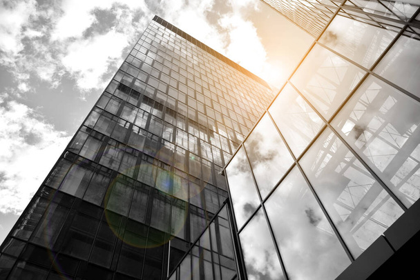 Πρόσοψη υφή ενός γυάλινου καθρέπτη κτιρίου γραφείων. Θραύσμα της πρόσοψης. Κάτω όψη των σύγχρονων ουρανοξύστες στην επιχειρηματική περιοχή στο φως το βράδυ στο ηλιοβασίλεμα με εφέ φλας φακού φίλτρο. Μαύρο και άσπρο. - Φωτογραφία, εικόνα