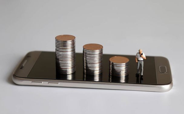 Smartphone a tři hromady mincí. Miniaturní lidé. - Fotografie, Obrázek