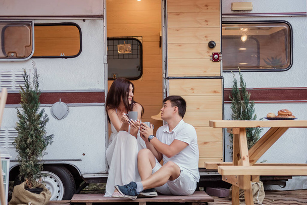 A beautiful couple drinks hot drinks for breakfast early in the morning, talking, looking at each other and laughing. The concept of rest in the country in a caravan. Honeymoon for Just Married - Фото, изображение