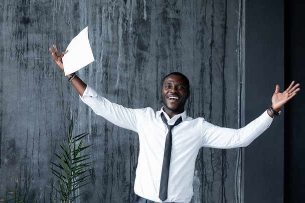 Employee in a white shirt spreading his arms joyfully to the sides and holding a white sheet of paper with a contract - Foto, afbeelding