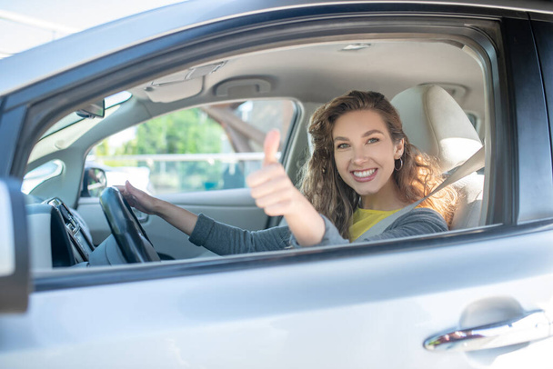Satisfied smiling woman driving car showing ok - Foto, afbeelding