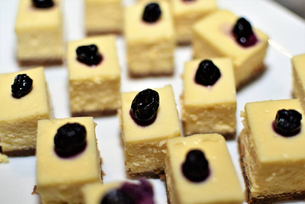Rebanadas de postre de pastel de queso con arándanos en la parte superior servido en un plato blanco
 - Foto, imagen