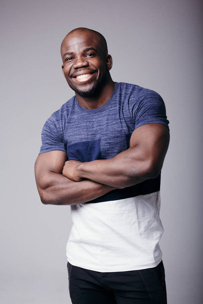 Portrait of a black man in a colored T-shirt holding his hands near his chest and smiling at the camera in the studio - Foto, Imagem