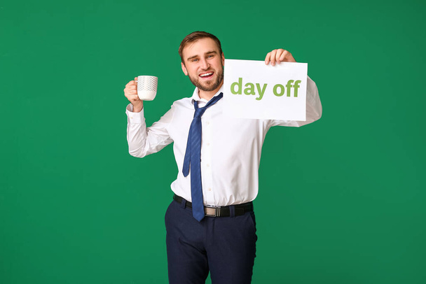 Young businessman with coffee holding paper with text DAY OFF against color background - Valokuva, kuva