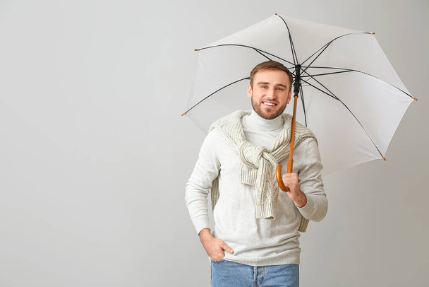 Όμορφος νεαρός άνδρας με ομπρέλα στο φως φόντο - Φωτογραφία, εικόνα