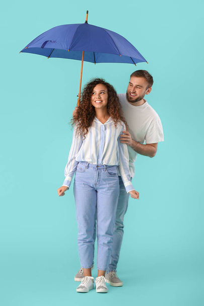 Happy young couple with umbrella on color background - Fotoğraf, Görsel